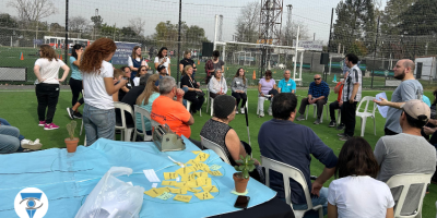 Charla de Tiflonexos. Se ve a dos personas hablando mientras muchas personas alrededor de ellos escuchan.